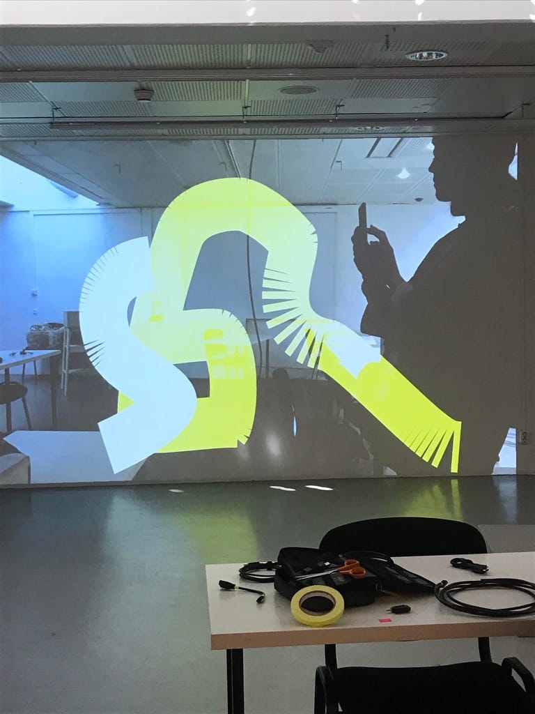 A projected image showing a persons silhouette holding a phone and two tangly shapes in yellow and white